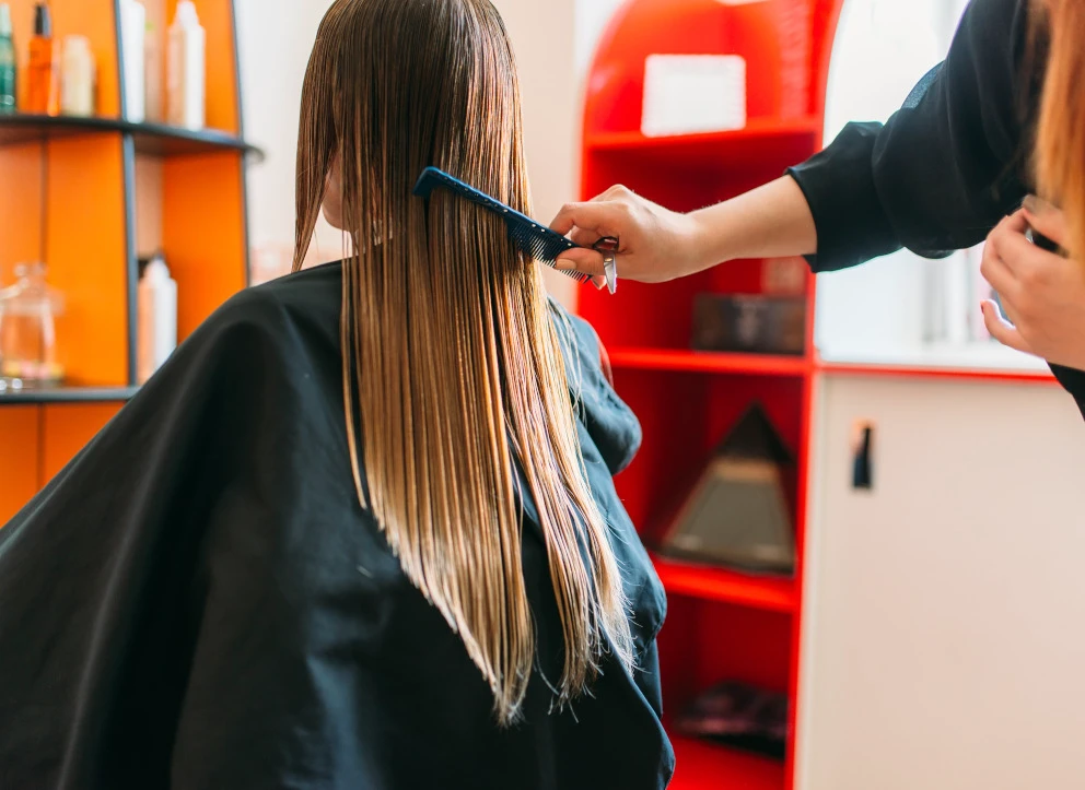 Eine Frisör schneidet die langen blonden Haare einer Frau in einem roten Salon