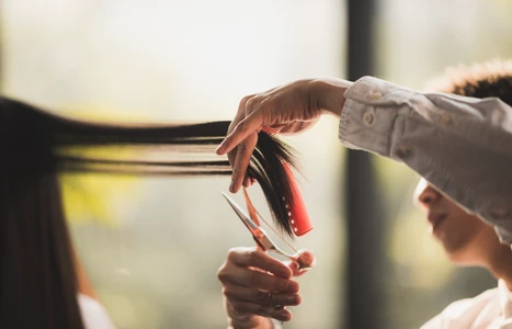 Ein Stylist schneidet mit Scheren einen Haarspitzenrand eines Kunden