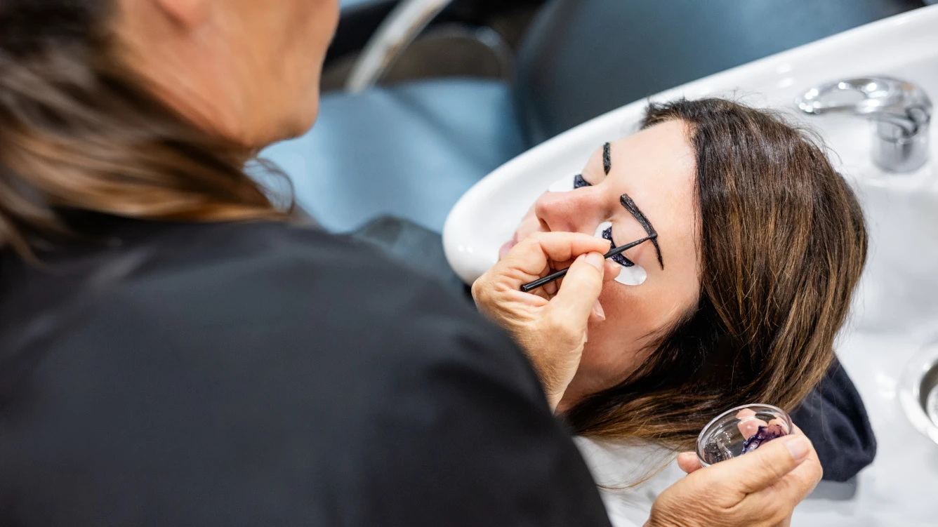 Eine Frau lächelt beim Haarwäschen in einem Salon während ein Stylist ihre Kopfhaut massiert